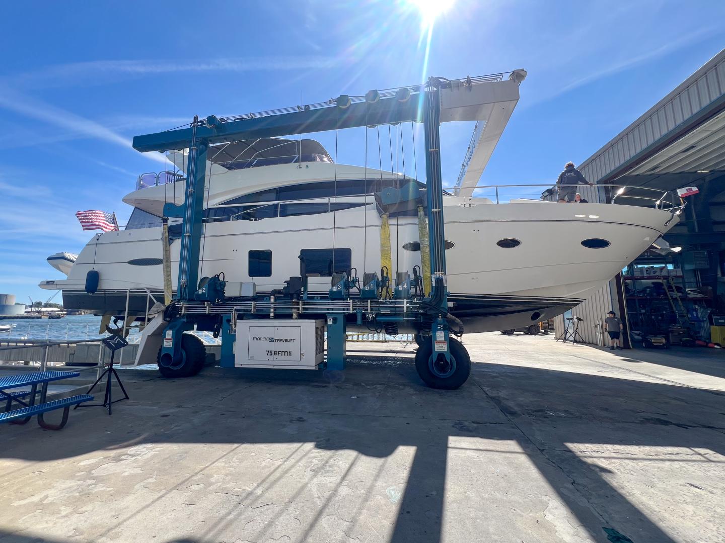 Large white yacht on a lift under a bright blue sky.