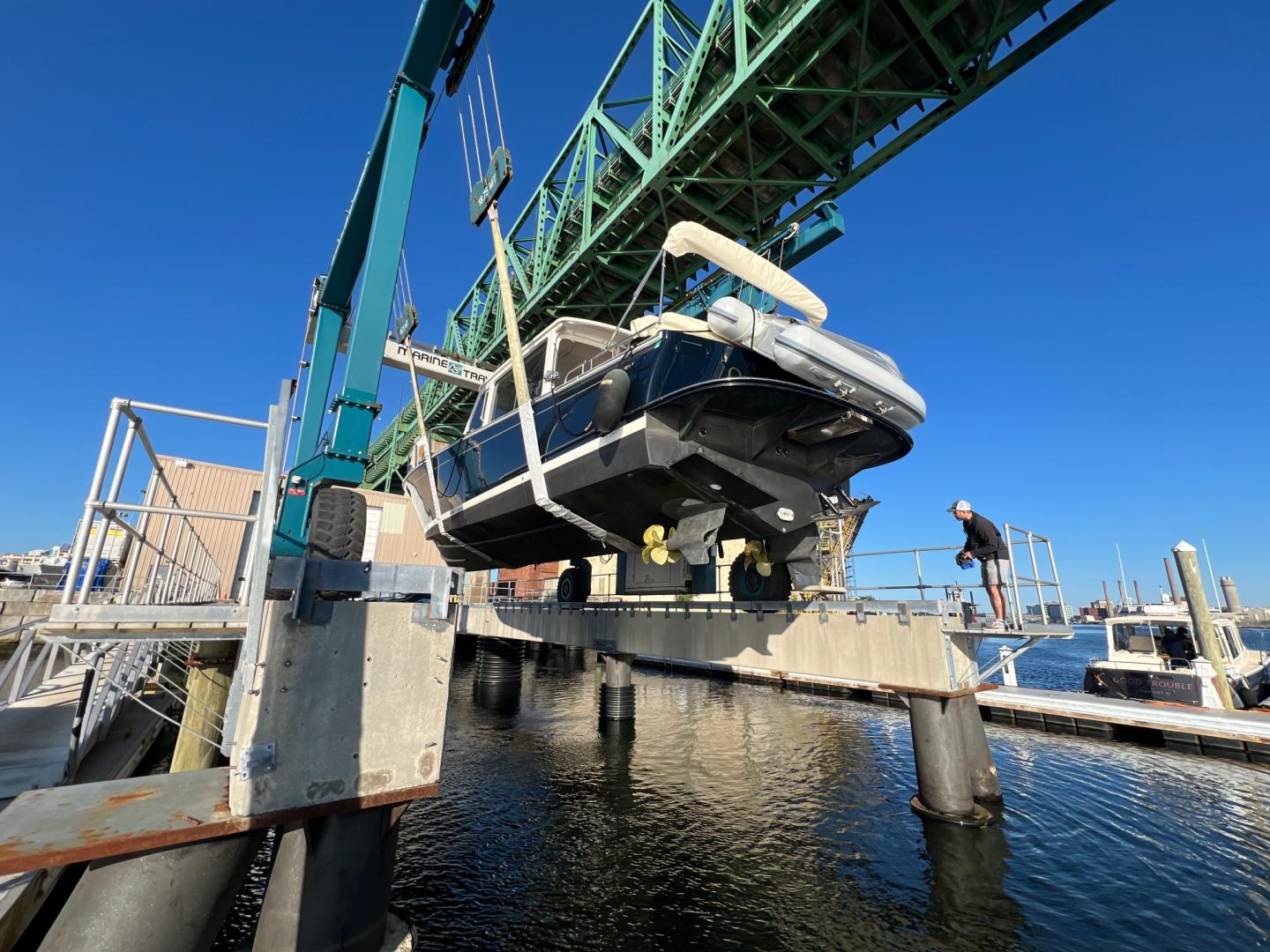 Boat being hoisted by a crane over a marina on a clear day.