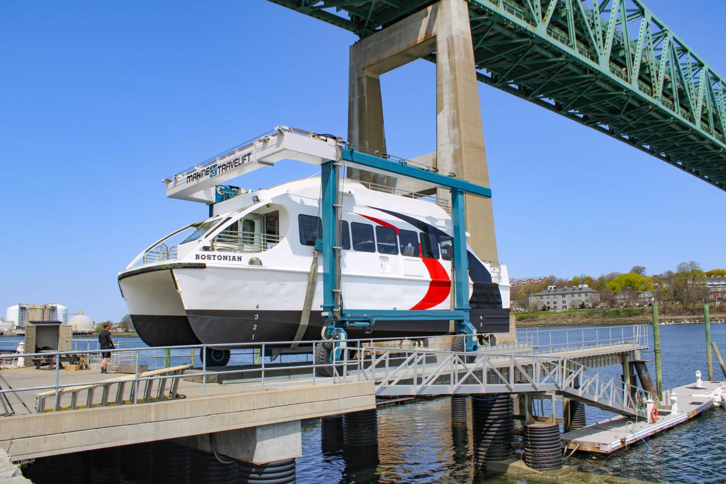 Ferry in dry dock under large bridge on a sunny day.