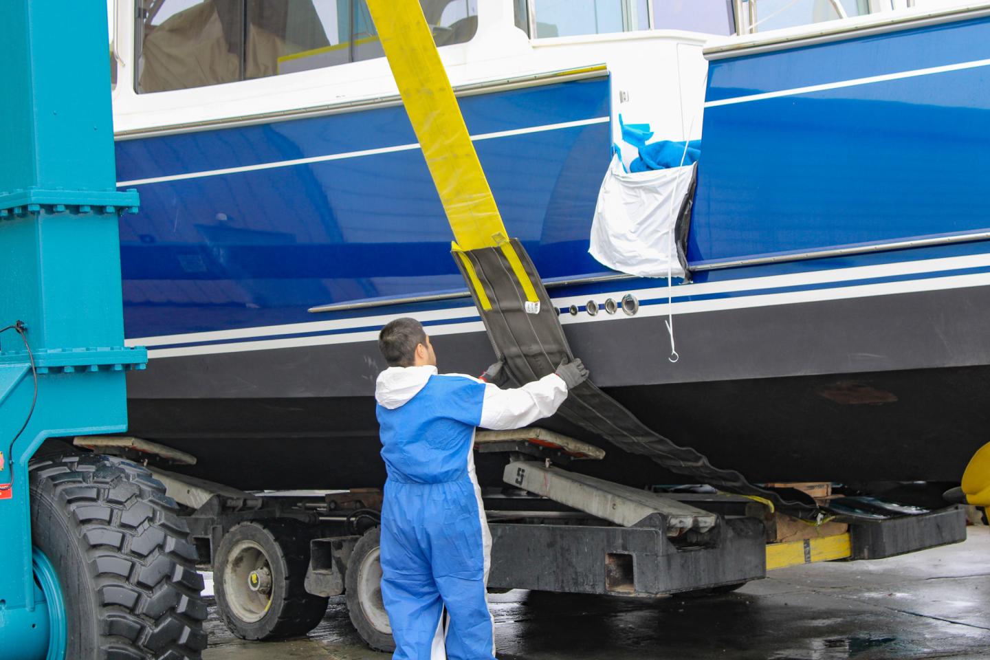 Worker in blue overalls adjusts straps lifting a blue boat.