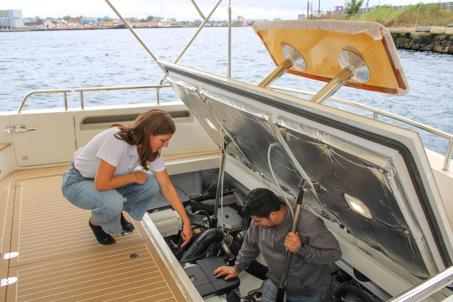 A woman and a man inspect a boat engine by the water.