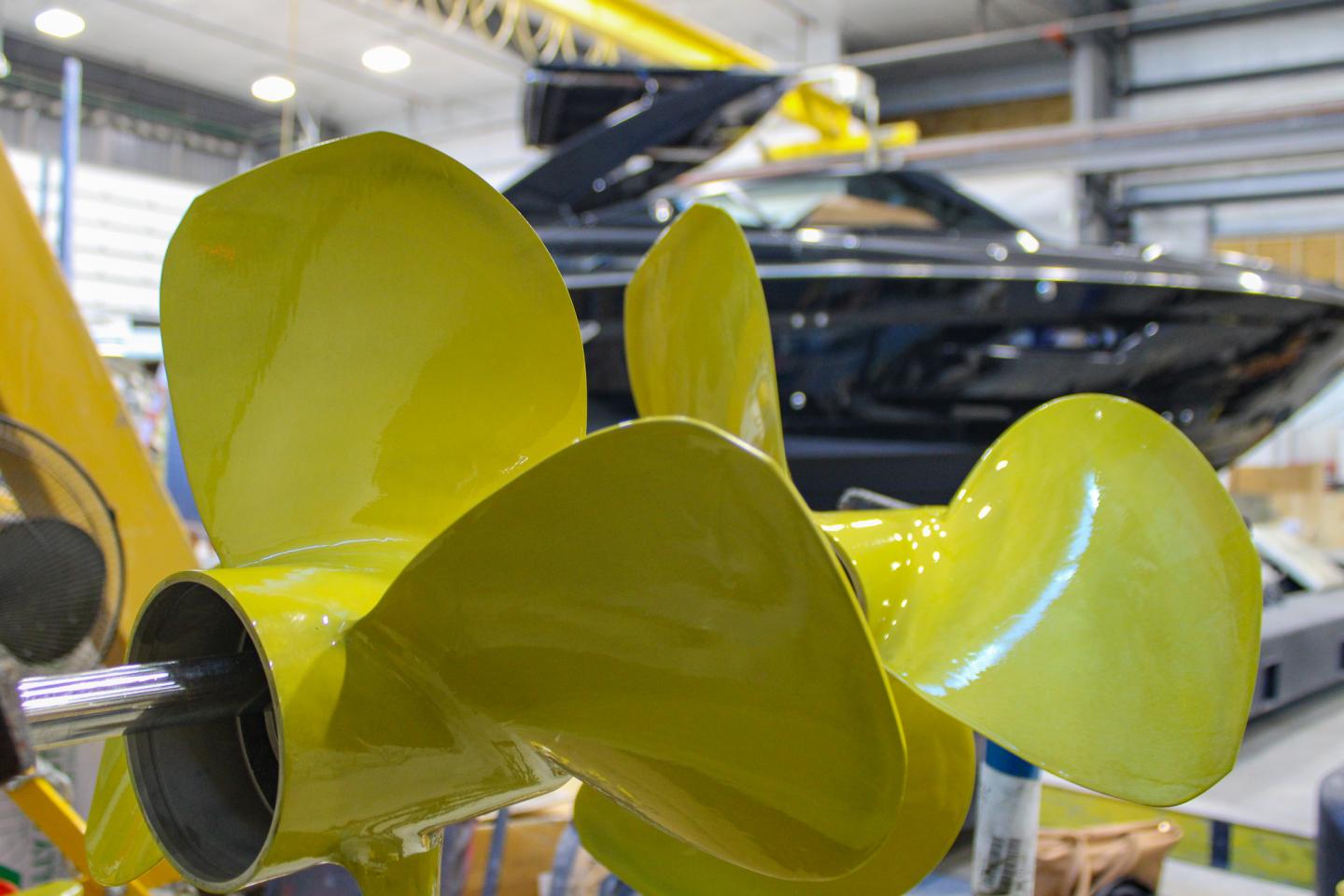 Yellow propeller in a workshop with a black boat in the background.