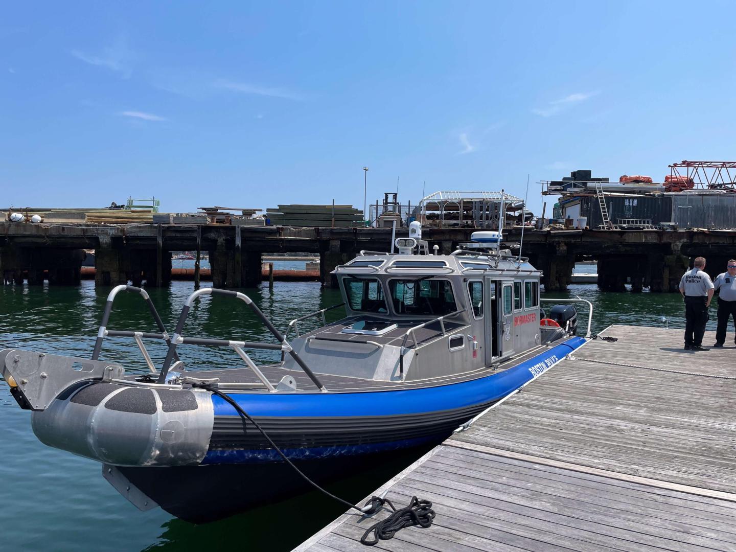 A docked police patrol boat with two people standing on the pier.