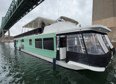 Green and white houseboat on a river under a bridge.